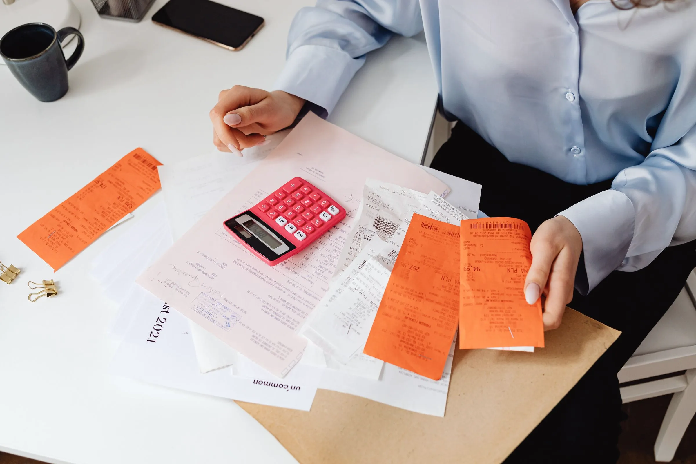 A pink calculator on a pile of invoices and receipts being sorted at a desk.