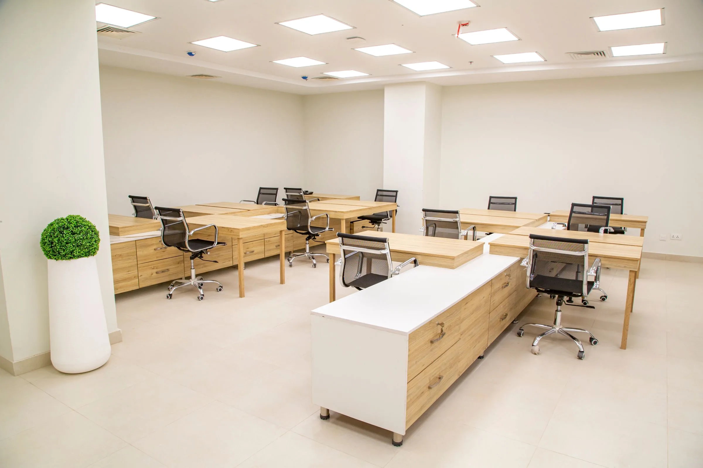 An empty modern office space with wooden desks, rolling chairs and a mobile storage unit.