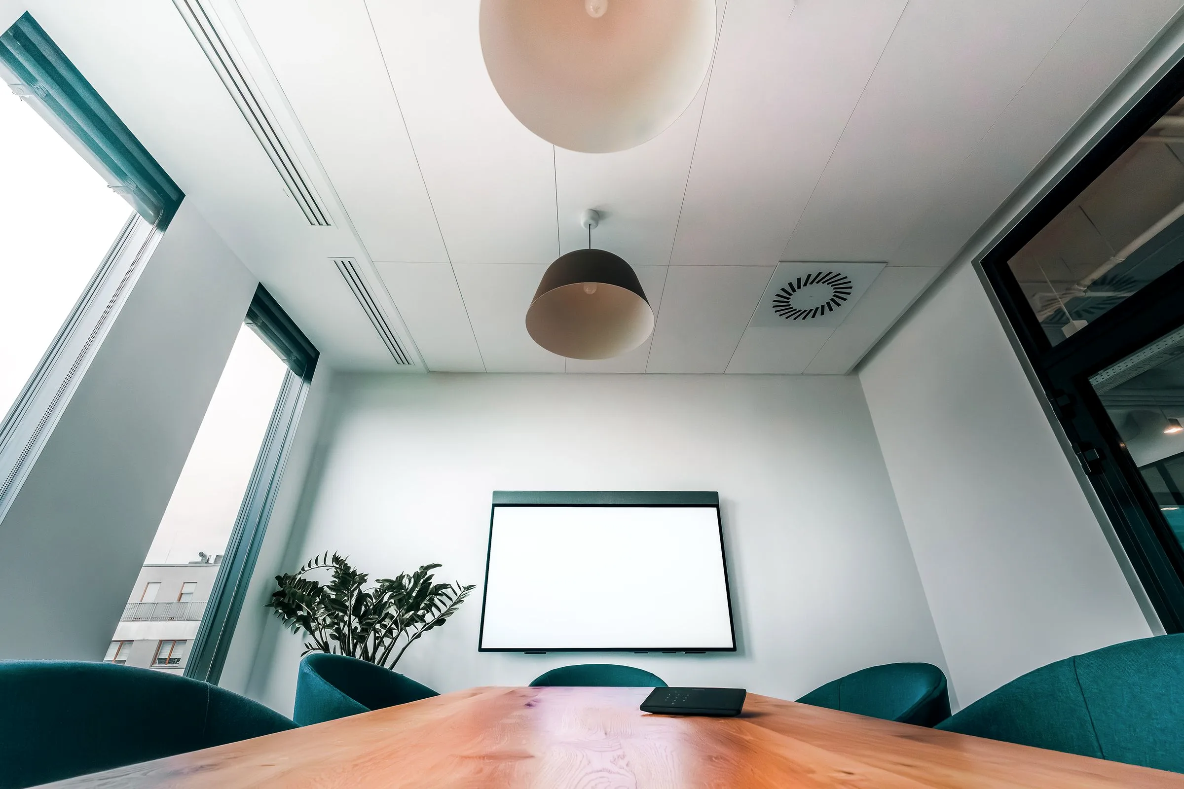 A bright, empty conference room with a blank wall screen and teal chairs.