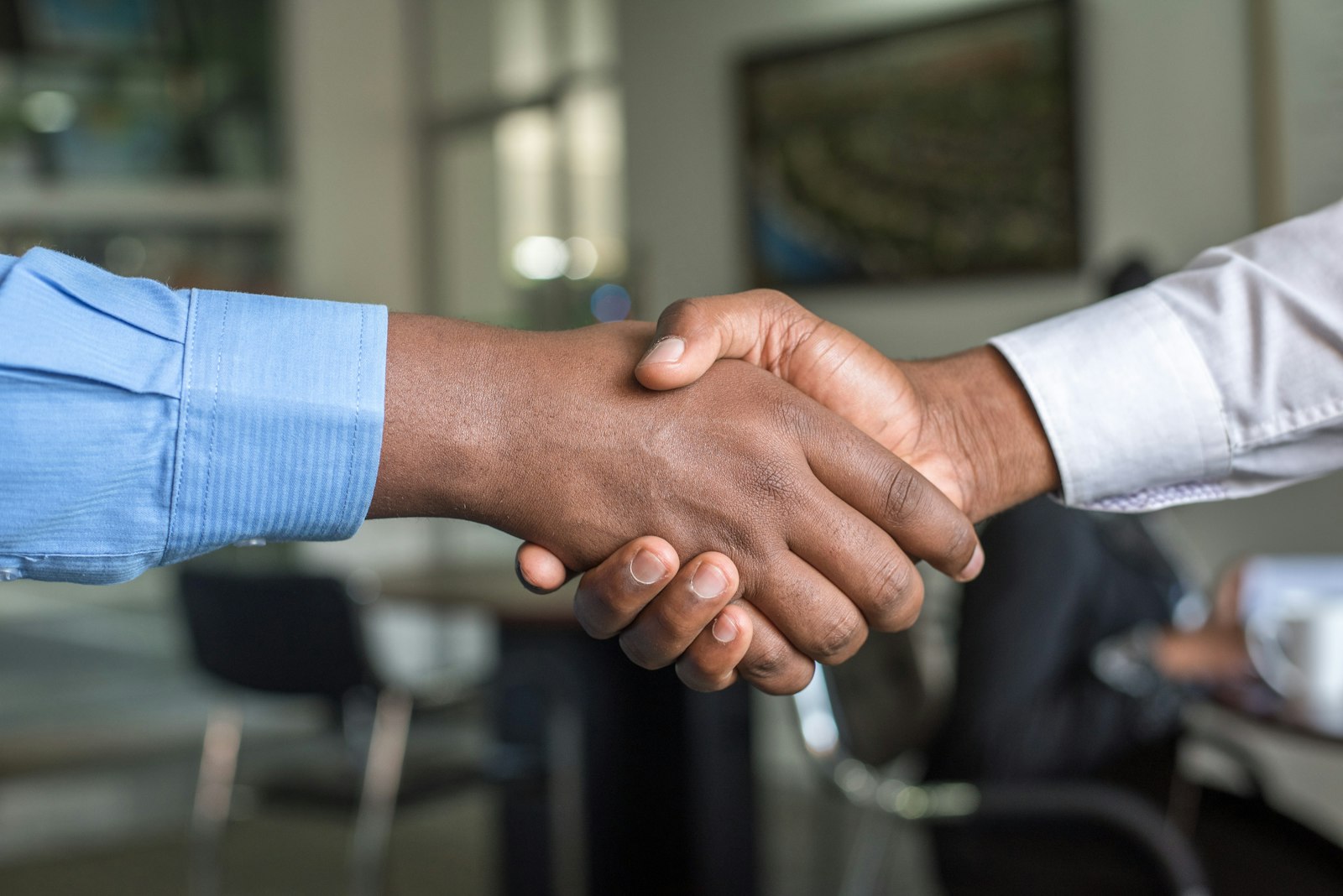 Cropped professional handshake, blue shirt sleeve, office backdrop