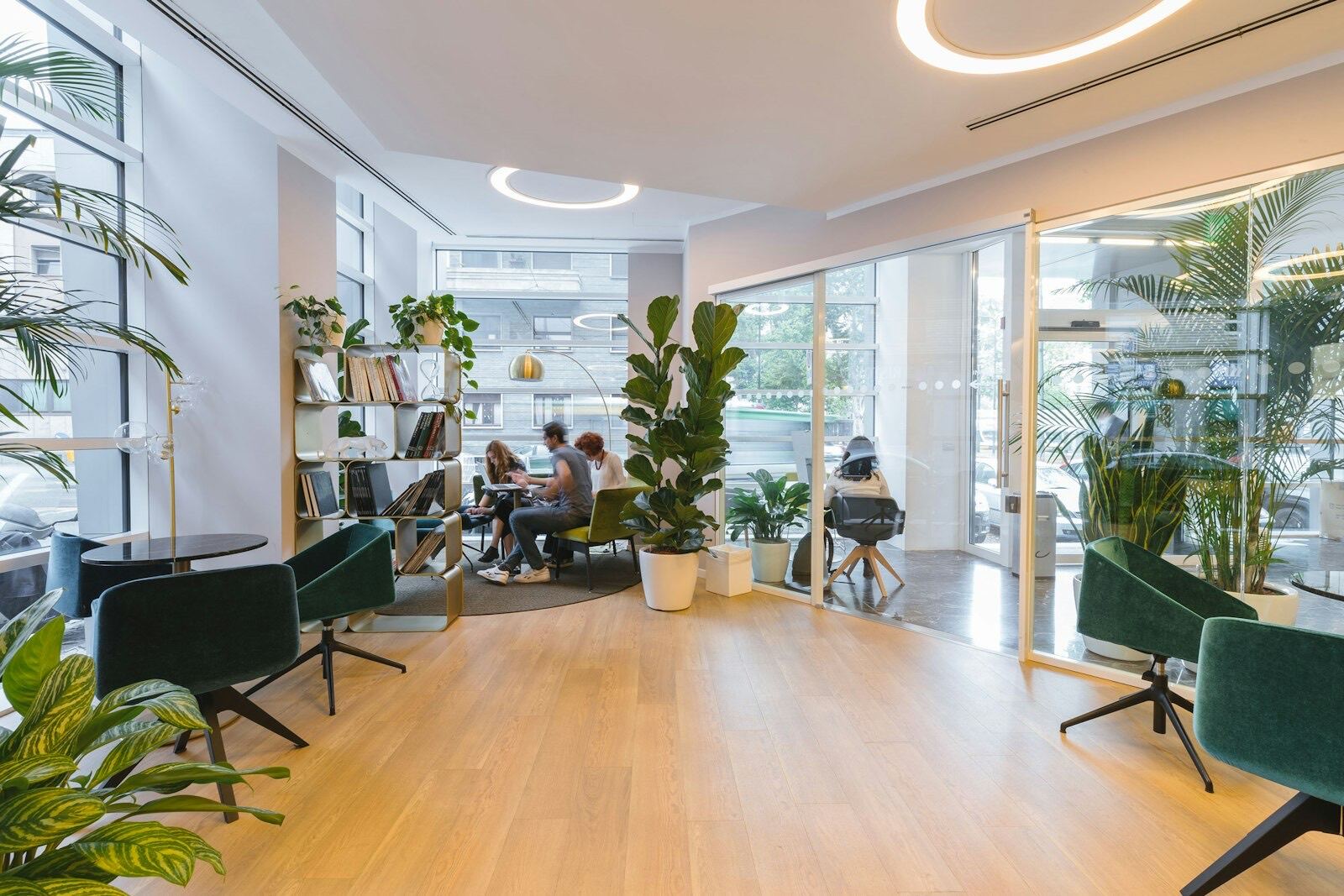 Bright modern office lounge with plants, glass partitions, and people working